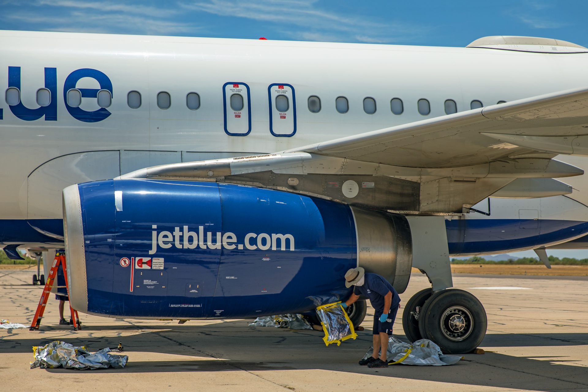 Maintenance crews remove engine covers from a JetBlue aircraft.